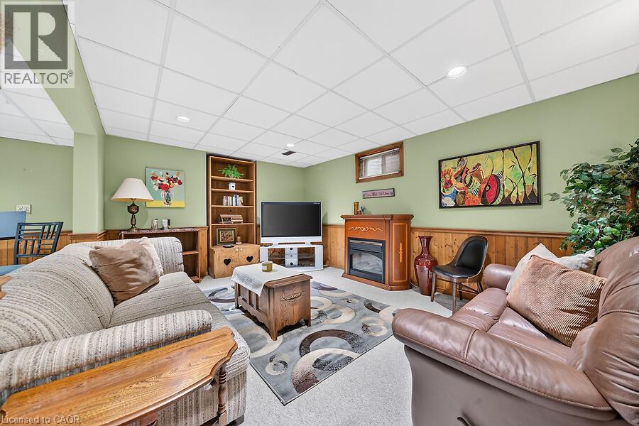 Recreation room featuring drop ceiling, recessed lighting, wood-finish wainscoting, light green walls, and a built-in fireplace with a decorative wood mantel - 30 Carriagegate Drive, Hamilton, ON - Indoor With Fireplace