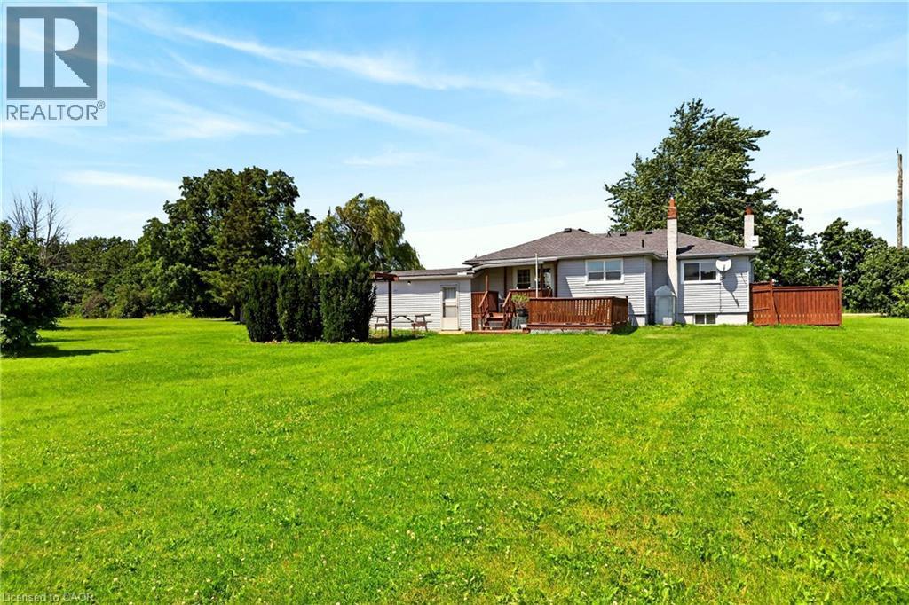 Expansive grassy lawn with mature perimeter trees, featuring a light grey exterior residence with a wood-tone deck and matching privacy fence - 958 Highland Road E, Hamilton, ON