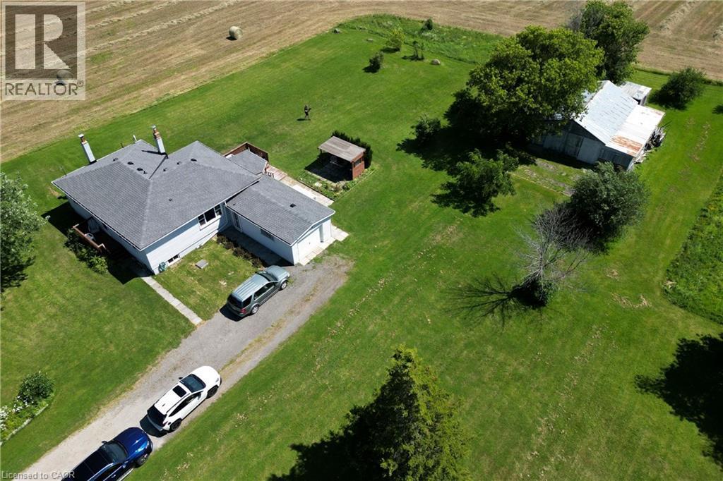 Expansive property featuring a grey-roofed residence with an attached garage, a detached outbuilding, a gravel driveway, and surrounding green lawn - 958 Highland Road E, Hamilton, ON