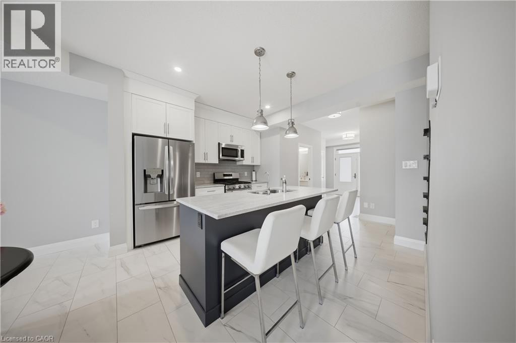 Modern kitchen featuring a central island with seating, white shaker-style cabinetry, stainless steel appliances, and a light-toned tiled floor - 107 Stephenson Way, Palmerston, ON - Indoor Photo Showing Kitchen With Stainless Steel Kitchen With Upgraded Kitchen
