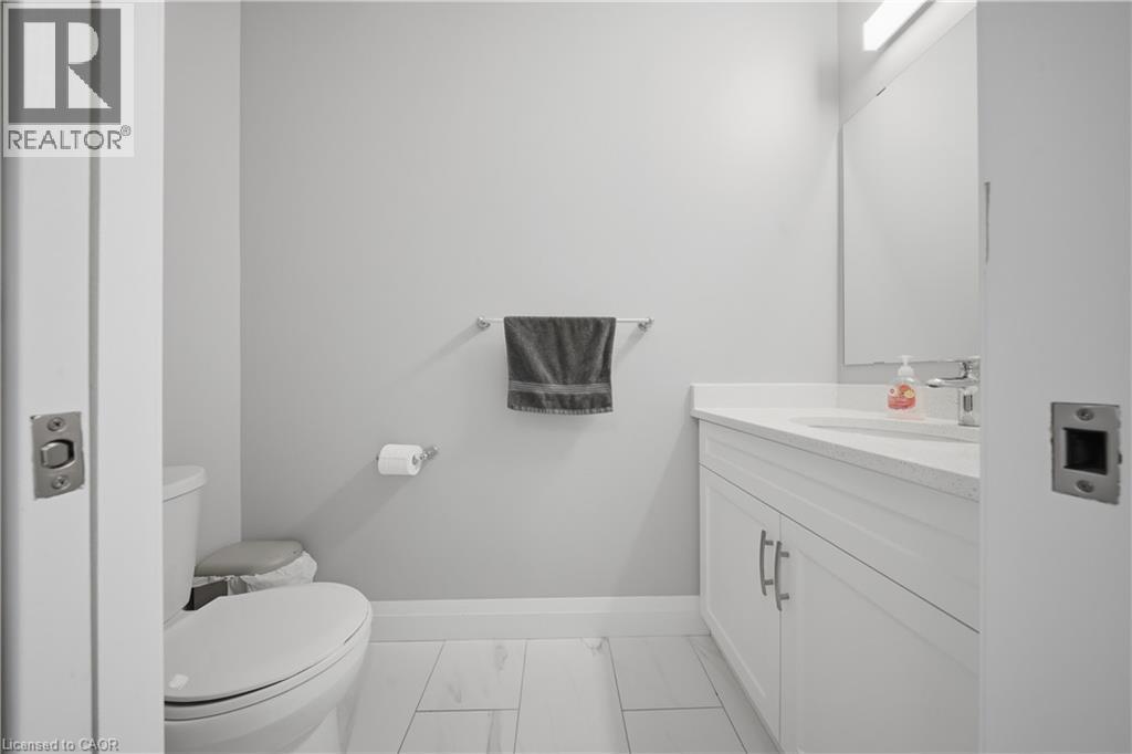 Bathroom featuring light gray walls, white wood-finish flooring, a white vanity with a light-toned countertop, a white toilet, and a wall-mounted mirror - 107 Stephenson Way, Palmerston, ON - Indoor Photo Showing Bathroom