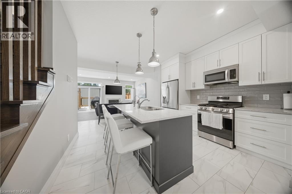 Open-concept kitchen featuring white shaker cabinetry, stainless steel appliances, a grey subway tile backsplash, and a central island with a light-colored countertop - 107 Stephenson Way, Palmerston, ON - Indoor Photo Showing Kitchen With Stainless Steel Kitchen With Double Sink With Upgraded Kitchen