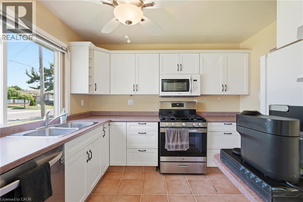 Kitchen featuring white cabinetry, a double basin stainless steel sink, tile flooring, a gas range, and a built-in microwave - 86 San Remo Drive, Hamilton, ON - Indoor Photo Showing Kitchen With Double Sink