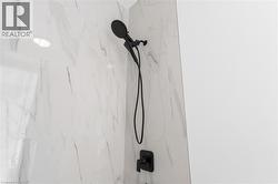Shower enclosure featuring large format white tile with grey veining, a matte black shower head, a handheld shower fixture, and a single-handle control -