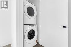 Dedicated laundry area featuring stacked appliances and a contemporary flat-panel door with matte black hardware -