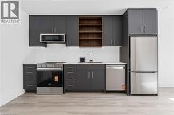 Modern kitchen featuring dark grey cabinetry, light-toned wood-finish flooring, and a full suite of stainless steel appliances including a refrigerator, range, microwave, and dishwasher -