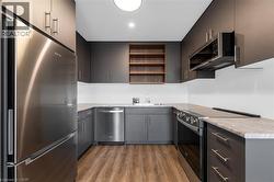 Modern kitchen featuring sleek grey cabinetry with brushed nickel hardware, stainless steel appliances, light-toned countertops, and wood-finish flooring -