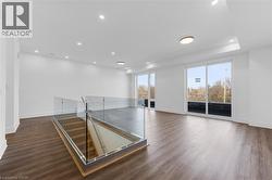 Spacious interior featuring wood-finish flooring, white walls, recessed ceiling lighting, glass railing, and multiple sliding glass doors -