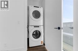 Compact laundry closet featuring a stacked white washer and dryer unit, dark wood-finish flooring, and a white interior door with matte black hardware -