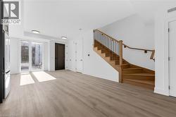 Open-concept living space with light wood-finish flooring, a modern wooden staircase with black iron balusters, white walls, and recessed lighting -