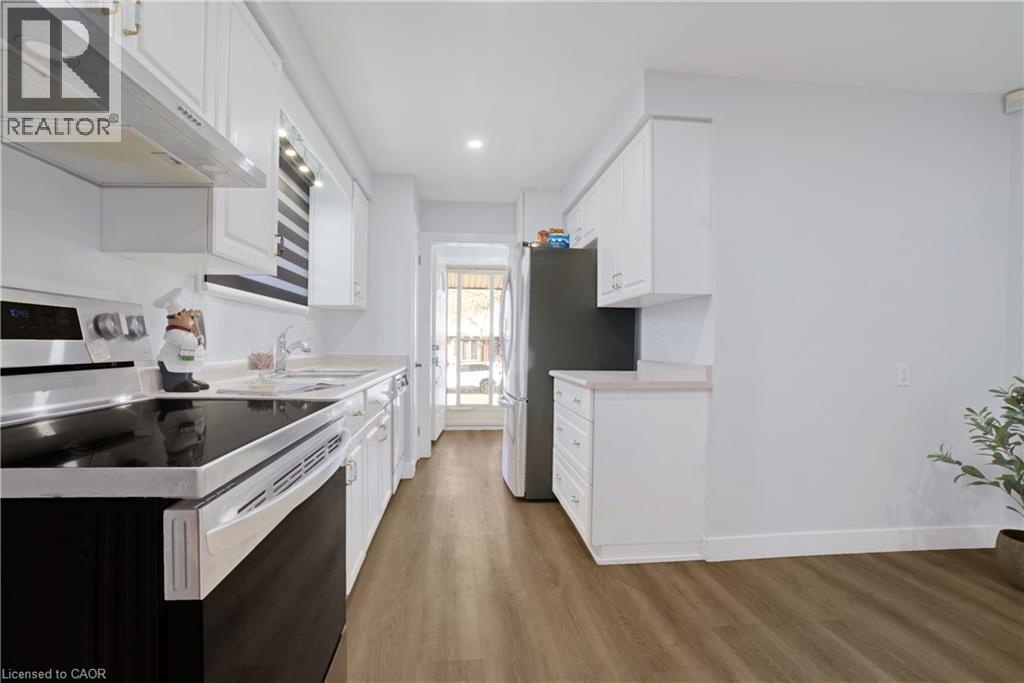 Galley kitchen featuring white cabinetry, light countertops, wood-finish flooring, a stainless steel range hood, and a black refrigerator - 60 Lysanda Avenue, London, ON - Indoor Photo Showing Kitchen