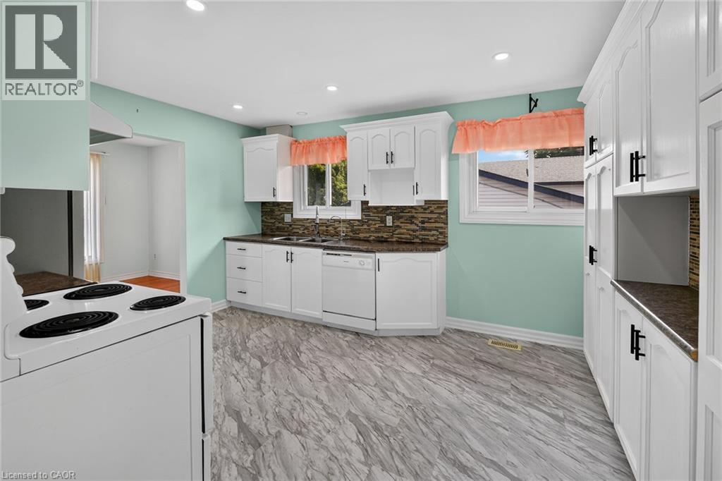 Bright kitchen featuring white cabinetry with dark hardware, stone-finish countertops, a mosaic tile backsplash, and wood-finish flooring - 186 Glenmor Drive, Caledonia, ON - Indoor Photo Showing Kitchen
