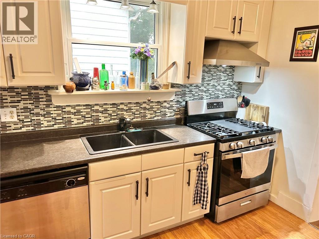 Kitchen featuring shaker-style cabinetry, mosaic tile backsplash, double basin sink, stainless steel appliances, and wood-finish flooring - 88 Brook Street, Simcoe, ON - Indoor Photo Showing Kitchen With Double Sink