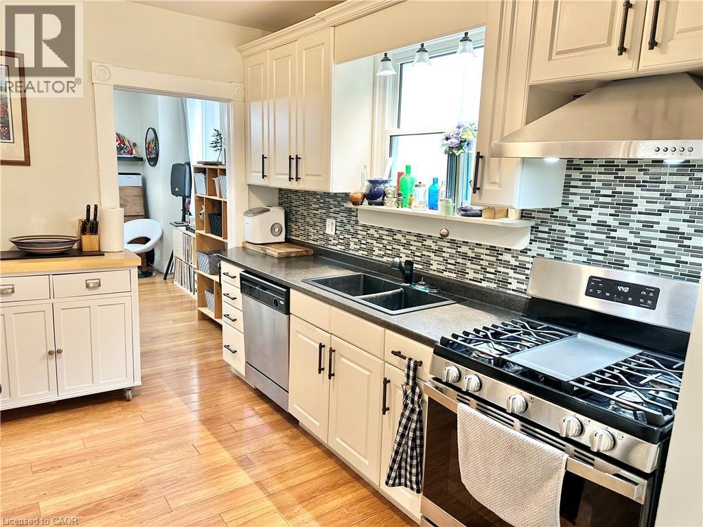 Kitchen featuring light wood-finish flooring, white cabinetry with dark hardware, a mosaic tile backsplash, stainless steel appliances, and a double basin sink - 88 Brook Street, Simcoe, ON - Indoor Photo Showing Kitchen With Double Sink With Upgraded Kitchen