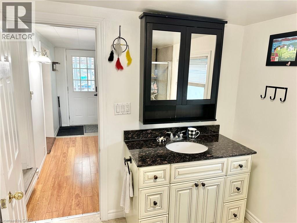 Bathroom vanity featuring a white oval sink, dark granite-style countertop, and distressed cream cabinetry - 88 Brook Street, Simcoe, ON - Indoor Photo Showing Bathroom