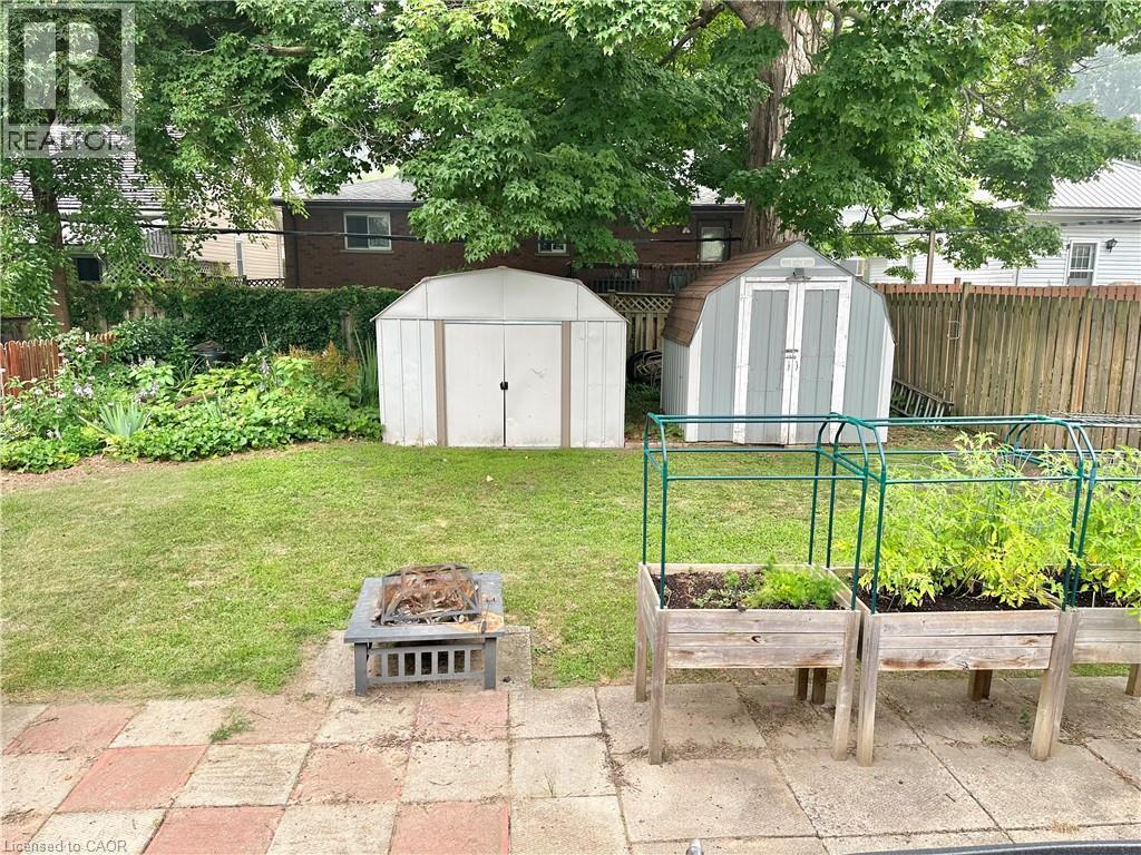 Expansive backyard featuring a lush lawn, two storage sheds, a stone patio, and raised garden beds - 88 Brook Street, Simcoe, ON - Outdoor