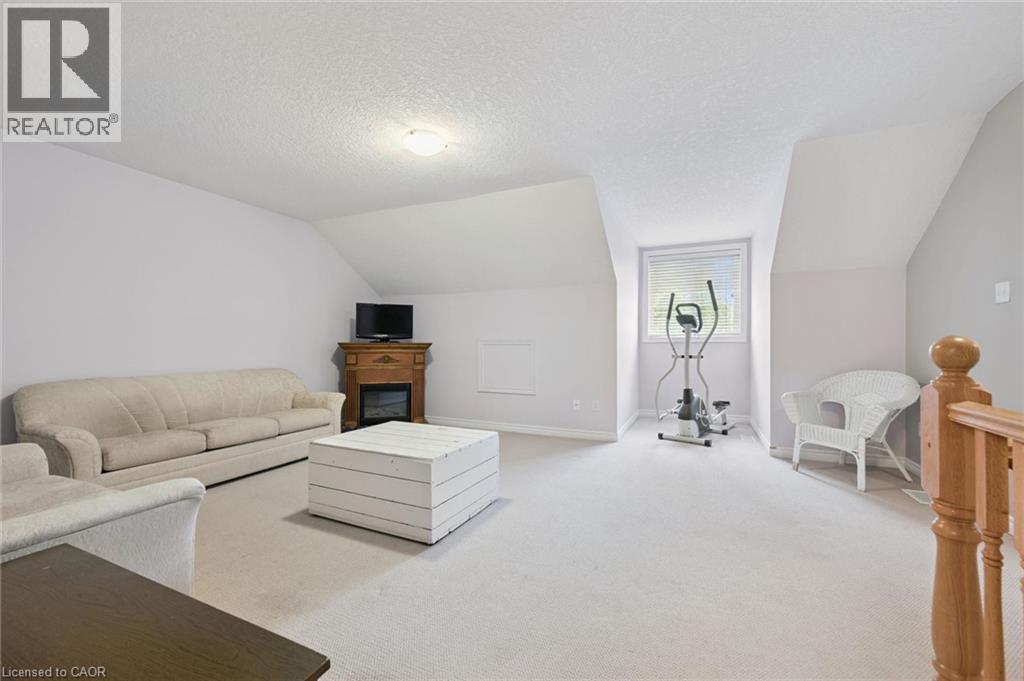 Spacious bonus room featuring sloped ceilings, light carpeting, a built-in electric fireplace with wood mantel, a large window, and a wood banister - 23 Knack Lane, Cambridge, ON - Indoor