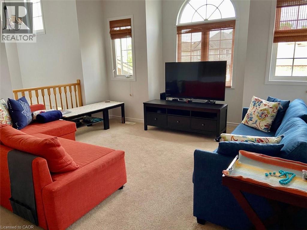 Open living area featuring neutral carpet flooring, an arched window, and additional windows with woven blinds - 287 Westmeadow Drive, Kitchener, ON - Indoor Photo Showing Living Room