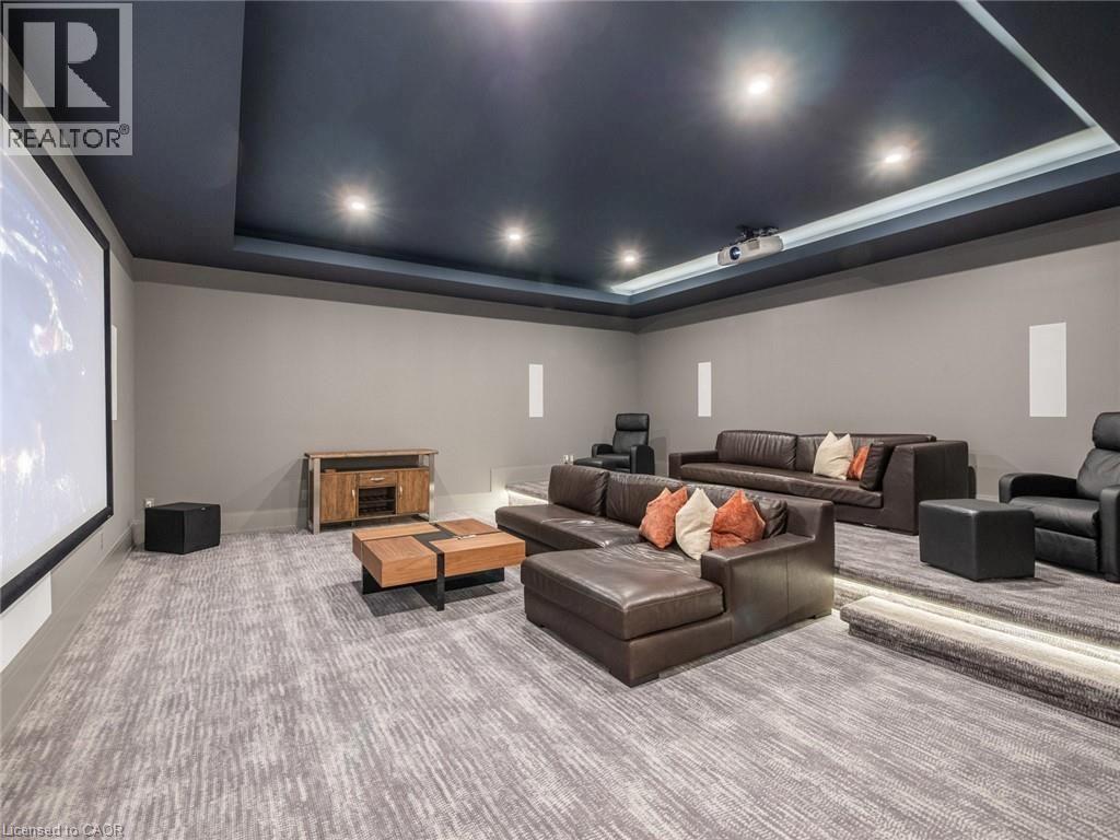 Dedicated media room featuring a large projection screen, recessed lighting, tiered seating platforms with integrated lighting, and patterned carpet flooring - 140 Secord Lane, Burlington, ON - Indoor