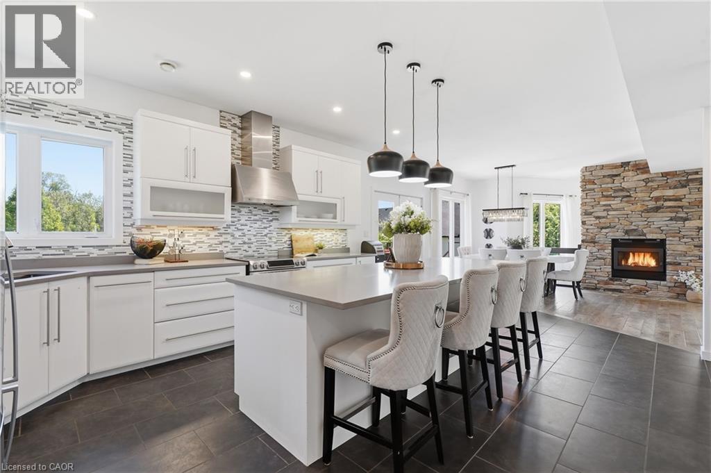 Modern kitchen featuring white cabinetry, a large center island with pendant lighting, stone-look backsplash, stainless steel appliances, and dark tile flooring - 5779 Third Line, Guelph/Eramosa, ON - Indoor Photo Showing Kitchen With Upgraded Kitchen