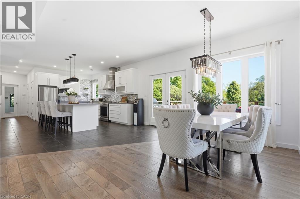 Open-concept living area featuring wood-finish flooring, a contemporary kitchen with white cabinetry and stainless steel appliances, a kitchen island with seating, and a dining area illuminated by a c - 5779 Third Line, Guelph/Eramosa, ON - Indoor Photo Showing Dining Room