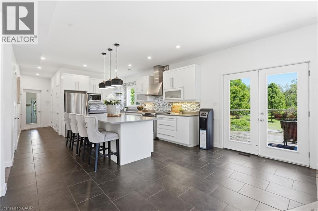 Open-concept kitchen featuring an island with pendant lighting, white cabinetry, stainless steel appliances, and a mosaic tile backsplash - 5779 Third Line, Guelph/Eramosa, ON - Indoor Photo Showing Kitchen With Stainless Steel Kitchen With Upgraded Kitchen