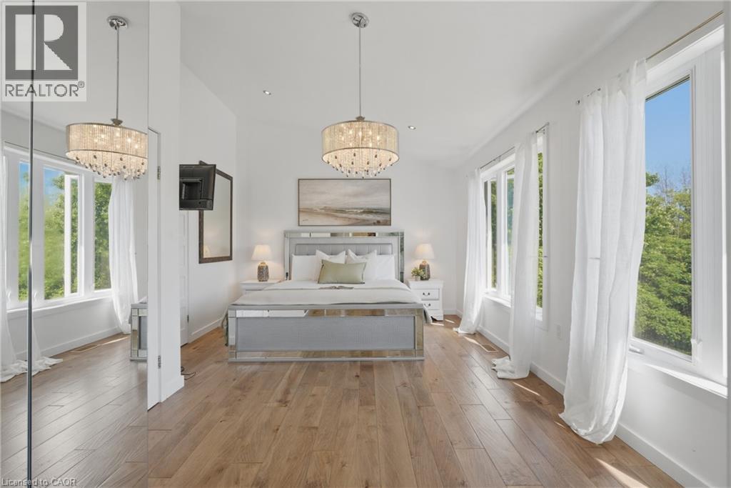 Spacious room featuring wood-finish flooring, multiple large windows, and a decorative chandelier - 5779 Third Line, Guelph/Eramosa, ON - Indoor