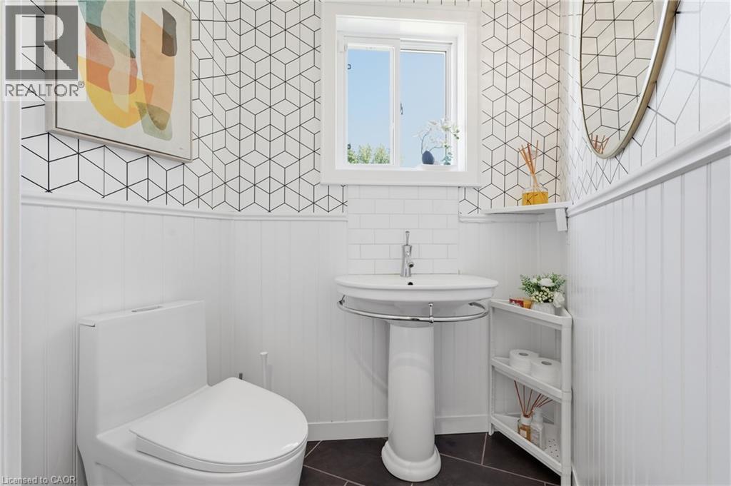 Powder room featuring a pedestal sink with chrome faucet, dark floor tiles, white wainscoting, and geometric pattern wallpaper - 5779 Third Line, Guelph/Eramosa, ON - Indoor Photo Showing Bathroom