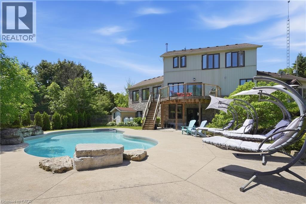 Irregularly shaped swimming pool with a concrete surround, rock features, and a stone retaining wall - 5779 Third Line, Guelph/Eramosa, ON - Outdoor With In Ground Pool With Backyard