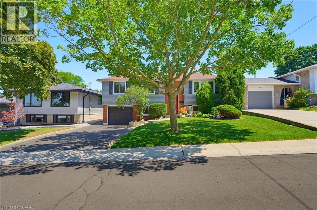 Exterior featuring gray siding, a dark garage door, and a well-maintained front lawn with mature landscaping - 164 Hanover Place, Hamilton, ON - Outdoor With Facade