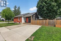 Exterior featuring red brick and dark siding, a prominent orange entry door, mature trees, a concrete driveway, and a wooden privacy fence -