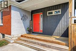 Exterior featuring a vibrant red entry door, vertical charcoal siding, painted white brick, and a wooden porch with steps -
