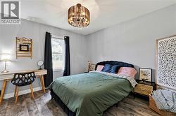 Neutral-toned room featuring wood-finish flooring, a double window with dark drapery, and a contemporary chandelier -