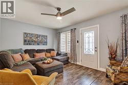 Living area featuring wood-finish flooring, a decorative front entry door with leaded glass, white window blinds, and a ceiling fan with integrated lighting -