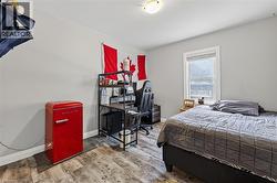 Bedroom featuring wood-finish flooring, light grey walls, white trim, and a single window with white blinds -