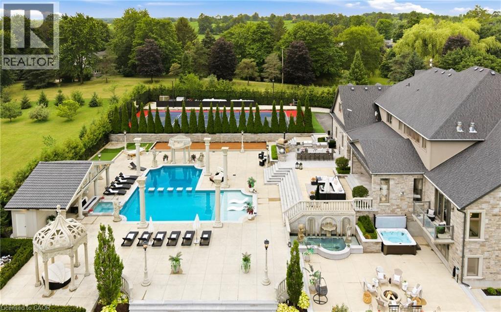 Expansive outdoor living area featuring a large swimming pool, multiple hot tubs, and a dedicated sports court - 7009 Wellington Rd 34, Puslinch, ON - Outdoor With In Ground Pool With View