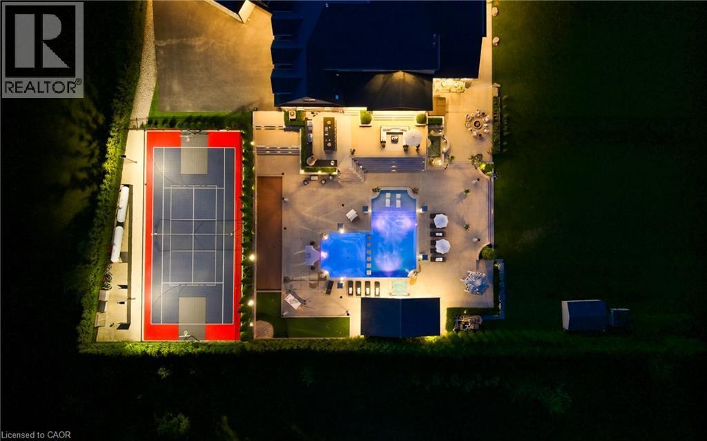 Expansive outdoor living area featuring a multi-sport court with perimeter lighting, a large illuminated swimming pool, extensive concrete patio space, and multiple shaded lounge areas - 7009 Wellington Rd 34, Puslinch, ON -