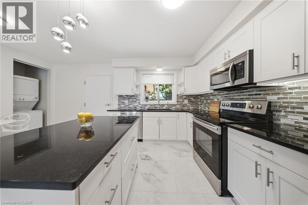 Modern kitchen featuring an expansive center island with dark countertops, white cabinetry, stainless steel appliances, a mosaic tile backsplash, and light-toned tile flooring - 80 Jackson Avenue, Kitchener, ON - Indoor Photo Showing Kitchen With Upgraded Kitchen