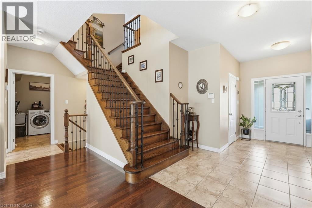 Two-story entryway featuring a hardwood staircase with dark iron balusters, a white front door with decorative glass inserts and side panels, and a combination of tile and wood-finish flooring - 1332 Baseline Road, Stoney Creek, ON - Indoor Photo Showing Other Room