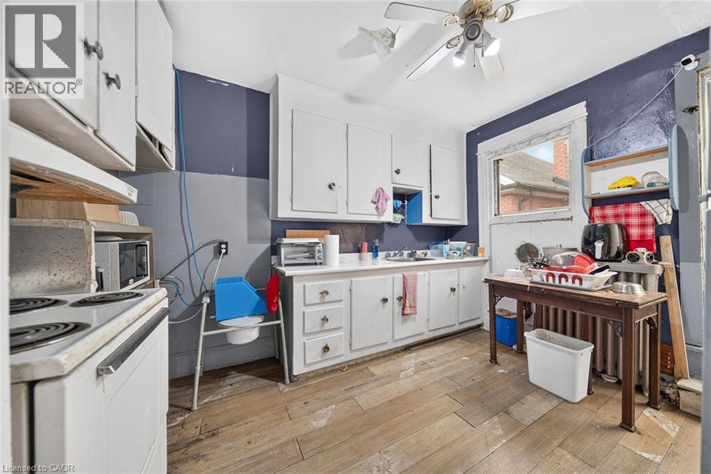 Kitchen featuring white cabinetry, a single basin sink, wood-finish flooring, and a ceiling fan with light fixture - 817 King Street E, Hamilton, ON