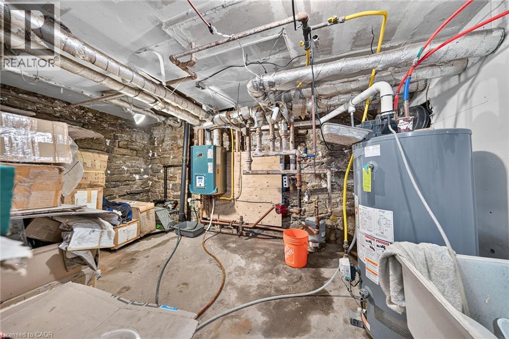 Utility room featuring a water heater, visible piping, and a stone foundation wall - 817 King Street E, Hamilton, ON