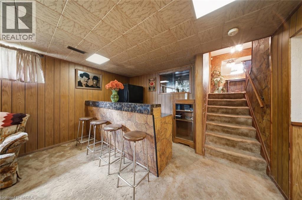 Lower-level entertainment space featuring a built-in bar with a stone-finish facade and a dark countertop, wood paneling, and a drop ceiling with integrated lighting - 1598 Highway No 6, Hamilton, ON - Indoor