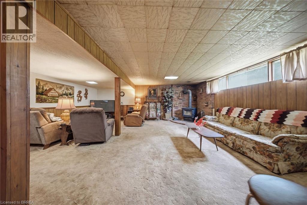 Spacious room featuring carpet flooring, wood paneling, a brick accent wall with a wood-burning stove, and overhead lighting - 1598 Highway No 6, Hamilton, ON - Indoor