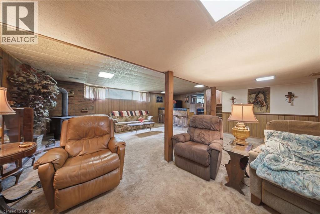 Carpeted recreation room featuring wood paneling, exposed wooden support beams, and a wood-burning stove with a brick surround - 1598 Highway No 6, Hamilton, ON - Indoor