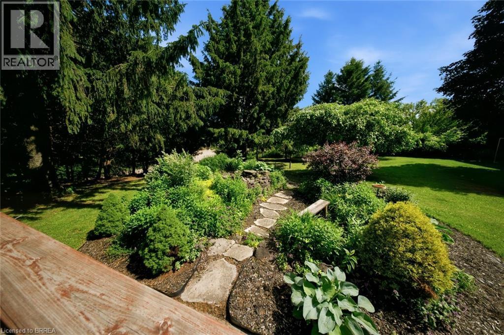 Manicured backyard featuring a stone-lined pathway, mature trees, diverse shrubs, and a built-in wooden bench - 1598 Highway No 6, Hamilton, ON - Outdoor