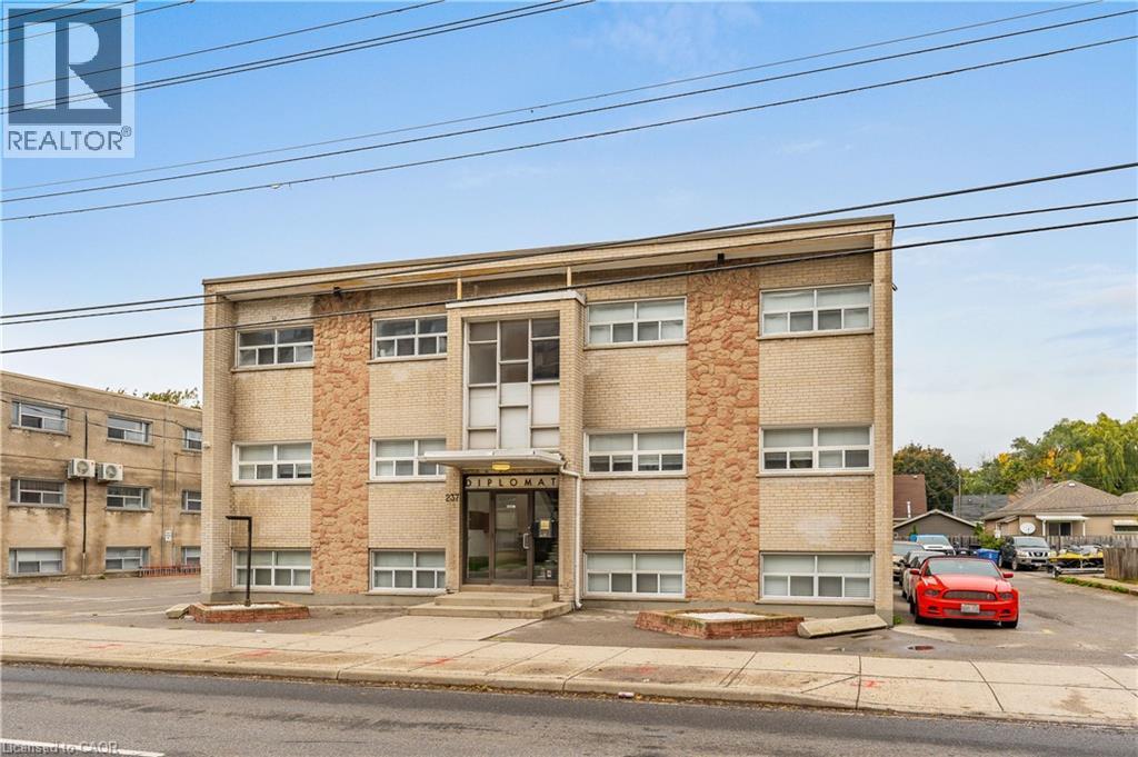 Three-story building featuring a concrete facade with stone veneer accents, multiple windows, and a prominent main entrance - 237 Mohawk Road E Unit# 16, Hamilton, ON - Outdoor