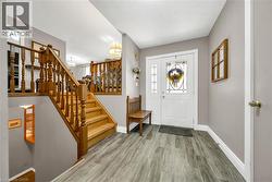 Foyer featuring wood-finish flooring, white entry door with decorative glass, white trim, and a wood staircase with balusters - 