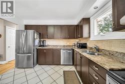 Kitchen featuring abundant brown cabinetry, stone countertops, a stainless steel French door refrigerator, and a double basin sink - 