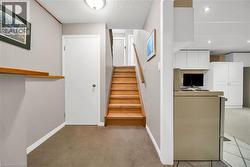 Lower level featuring a wood-finish staircase, light-colored carpeting, a partition wall with a wood-finish ledge, and a ceiling-mounted light fixture - 