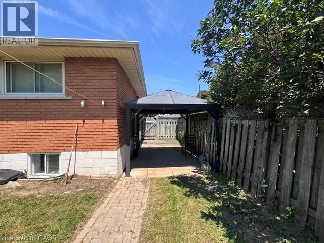 Exterior of the property featuring brick and block construction, a ground-level window, and a paved walkway leading to a covered patio area - 90 Anna Capri Drive Unit# Lower, Hamilton, ON - Outdoor With Exterior